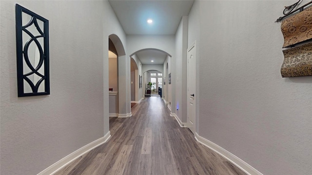 hall featuring arched walkways, wood finished floors, and baseboards