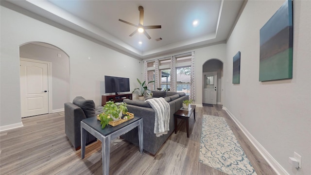 living area featuring light wood finished floors, baseboards, arched walkways, and a tray ceiling