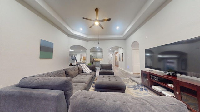 living area featuring arched walkways, recessed lighting, wood finished floors, a ceiling fan, and a raised ceiling