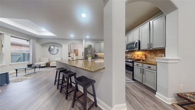 kitchen featuring arched walkways, decorative backsplash, a kitchen breakfast bar, wood finished floors, and stainless steel appliances