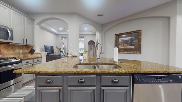 kitchen with light stone counters, gray cabinets, decorative backsplash, appliances with stainless steel finishes, and a sink