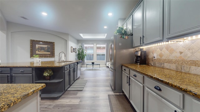 kitchen with light wood finished floors, a skylight, dark stone counters, freestanding refrigerator, and a sink