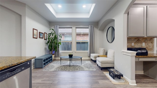 sitting room featuring a skylight, light wood finished floors, recessed lighting, a raised ceiling, and baseboards