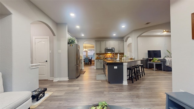 kitchen with arched walkways, a breakfast bar, gray cabinets, stainless steel appliances, and light wood-style floors