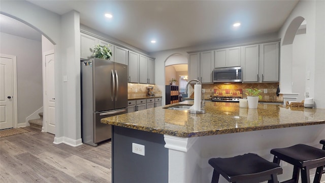 kitchen with arched walkways, stainless steel appliances, a sink, and dark stone counters