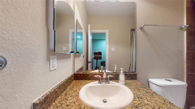 bathroom with toilet, vanity, and a textured wall