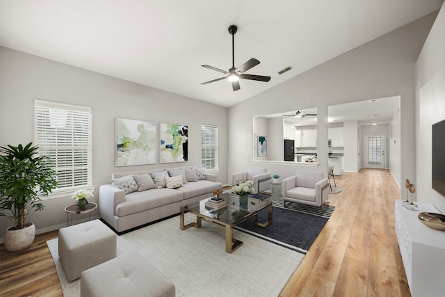 living room featuring lofted ceiling, visible vents, baseboards, a ceiling fan, and light wood-type flooring