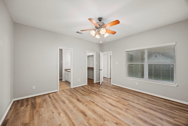 unfurnished bedroom with ensuite bathroom, light wood-style flooring, baseboards, a spacious closet, and a closet