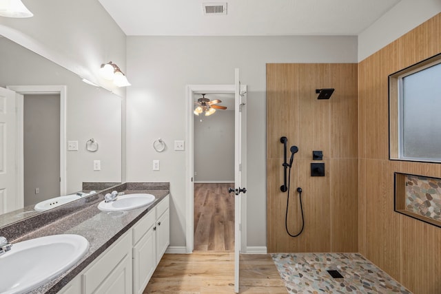 bathroom with wood finished floors, tiled shower, a sink, and visible vents