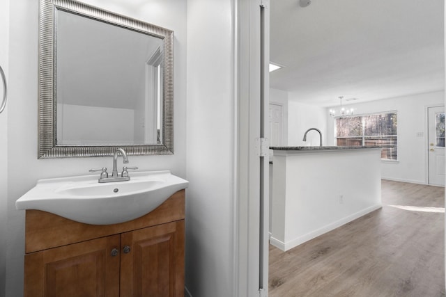 bathroom with baseboards, wood finished floors, vanity, and a notable chandelier