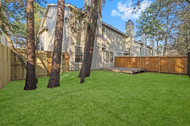 rear view of property with a fenced backyard, a lawn, a chimney, and a wooden deck