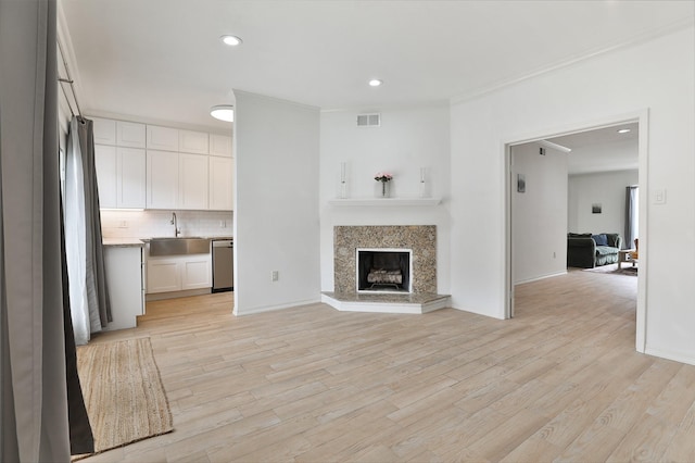 unfurnished living room featuring crown molding, light wood finished floors, visible vents, a premium fireplace, and a sink