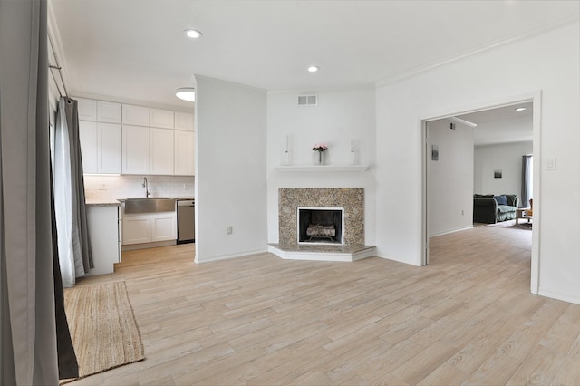 unfurnished living room featuring light wood finished floors, recessed lighting, a sink, crown molding, and visible vents