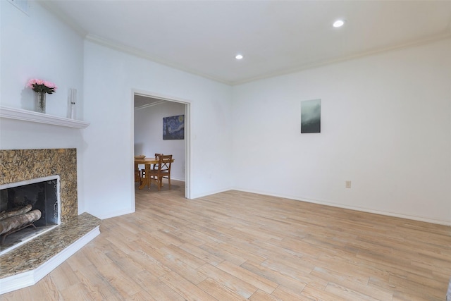 unfurnished living room featuring baseboards, light wood-type flooring, a fireplace, and crown molding