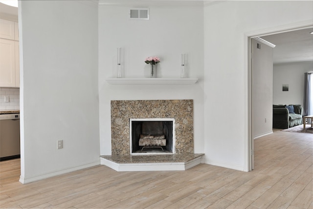 unfurnished living room featuring light wood-style flooring, ornamental molding, a fireplace, baseboards, and visible vents