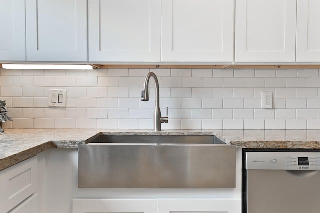 kitchen featuring light stone counters, a sink, white cabinets, stainless steel dishwasher, and backsplash