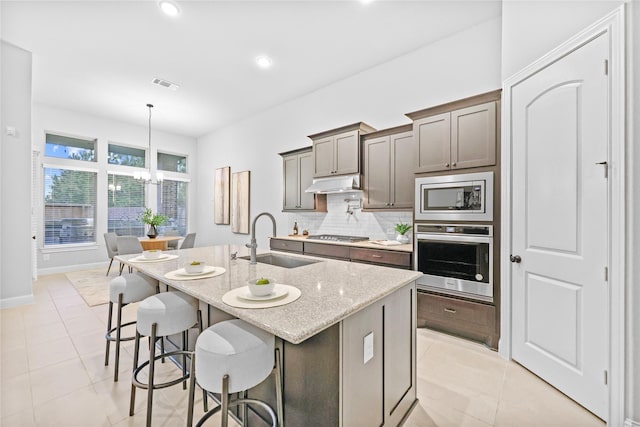 kitchen with light tile patterned floors, under cabinet range hood, a sink, visible vents, and appliances with stainless steel finishes