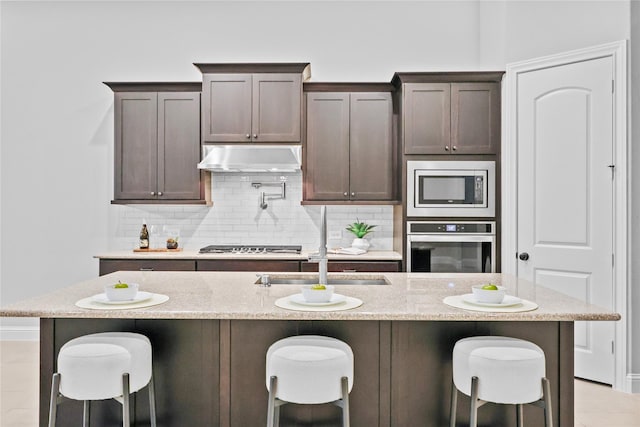 kitchen featuring appliances with stainless steel finishes, backsplash, dark brown cabinetry, and under cabinet range hood