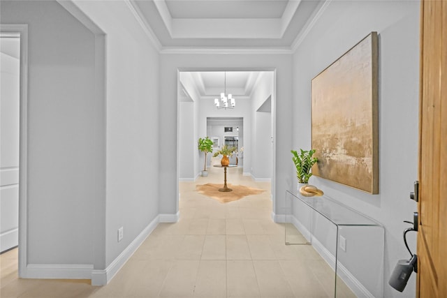 corridor with light tile patterned floors, baseboards, ornamental molding, a tray ceiling, and a chandelier