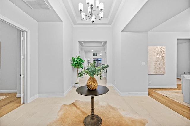 entryway featuring a chandelier, wood finished floors, visible vents, baseboards, and ornamental molding