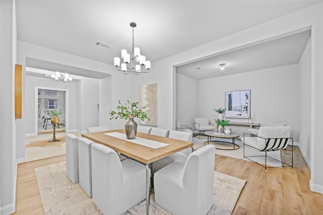 dining area featuring baseboards, visible vents, a notable chandelier, and light wood finished floors