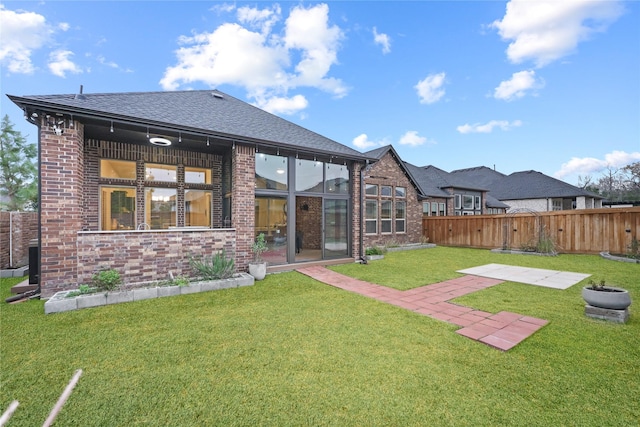 back of house featuring brick siding, a lawn, and fence