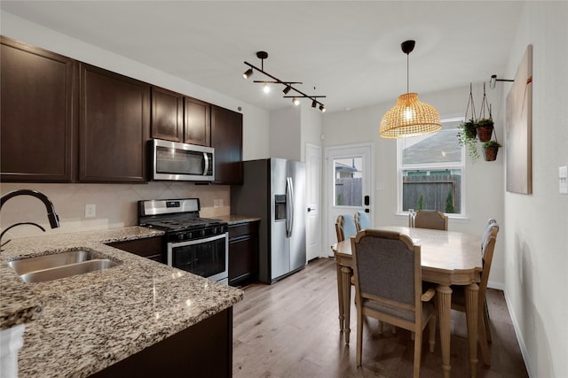 kitchen featuring dark brown cabinetry, stainless steel appliances, a sink, light wood-type flooring, and backsplash