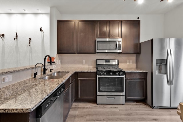 kitchen featuring light wood-type flooring, appliances with stainless steel finishes, dark brown cabinets, and a sink