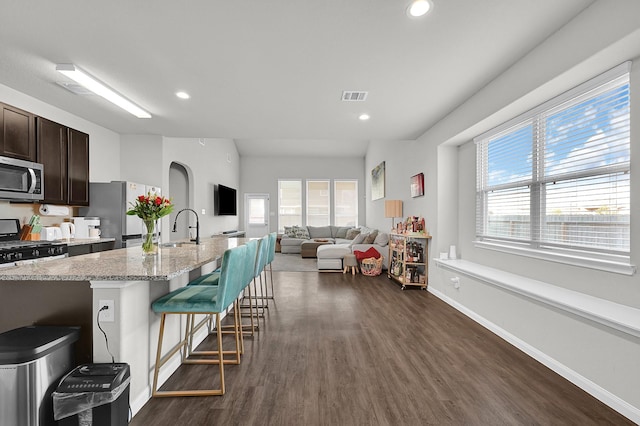 kitchen featuring dark brown cabinetry, dark wood-type flooring, stainless steel appliances, a kitchen bar, and a sink