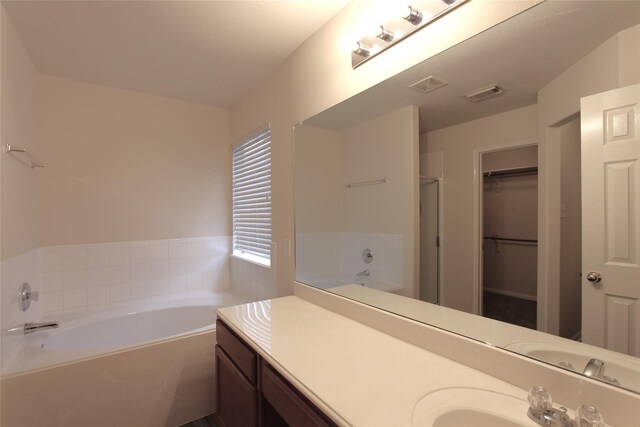 bathroom featuring visible vents, a garden tub, vanity, and a spacious closet