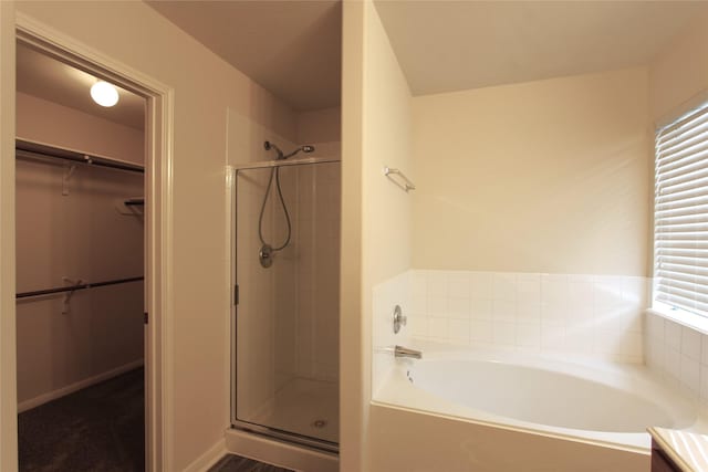 bathroom featuring a garden tub, a shower stall, baseboards, and a walk in closet