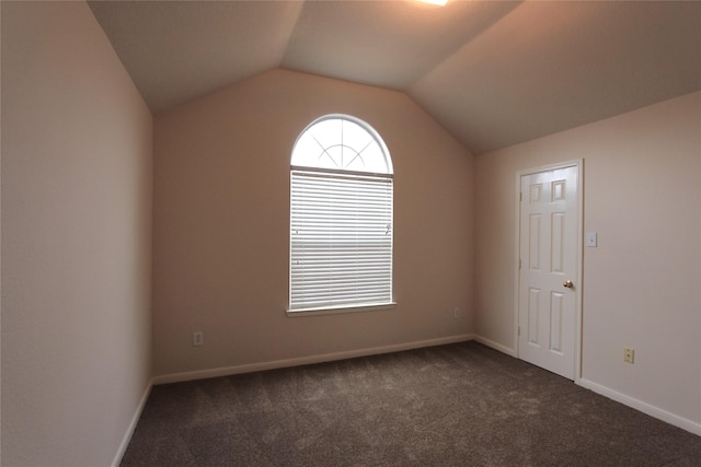 spare room with baseboards, dark carpet, and vaulted ceiling