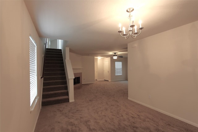 unfurnished living room featuring carpet, a fireplace, stairway, baseboards, and ceiling fan with notable chandelier