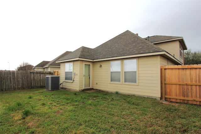 back of property with a shingled roof, a fenced backyard, a yard, and central AC unit