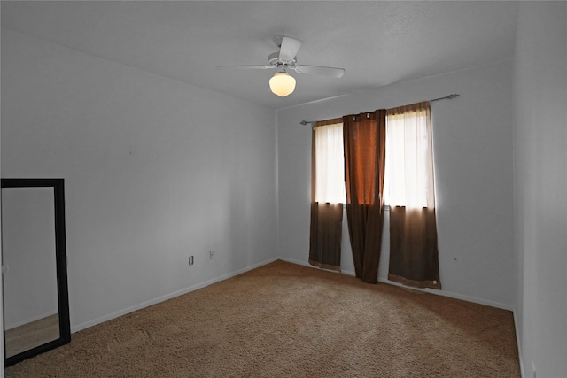 carpeted spare room featuring ceiling fan and baseboards