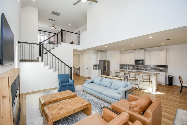 living area with visible vents, light wood-style flooring, a high ceiling, a ceiling fan, and stairs