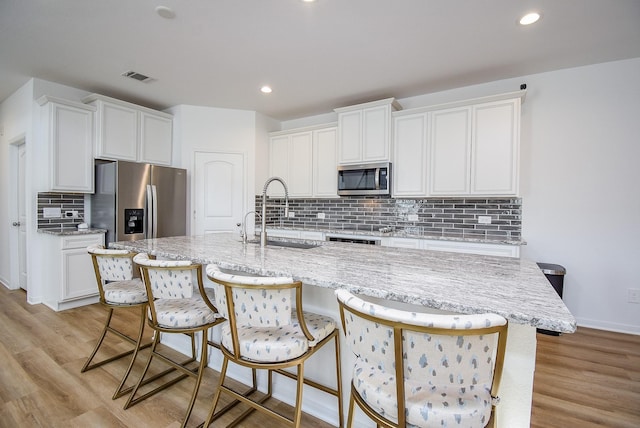 kitchen featuring visible vents, white cabinets, stainless steel appliances, light wood-type flooring, and a sink