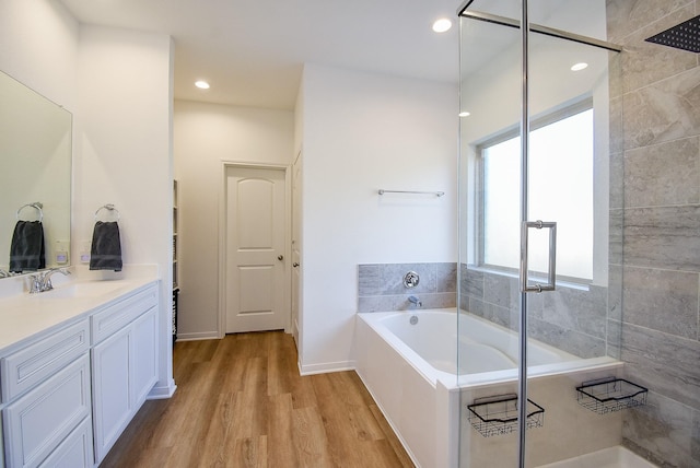 bathroom with a stall shower, wood finished floors, vanity, a bath, and recessed lighting