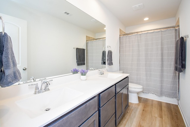 bathroom with double vanity, visible vents, toilet, a sink, and wood finished floors