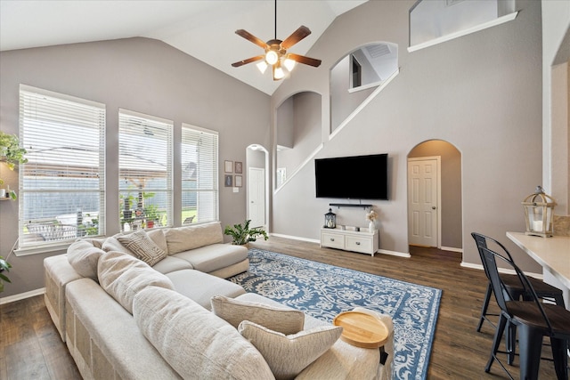 living area featuring arched walkways, high vaulted ceiling, wood finished floors, and baseboards