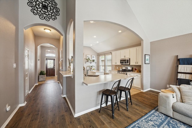 kitchen featuring dark wood-style flooring, a breakfast bar area, stainless steel appliances, open floor plan, and white cabinetry