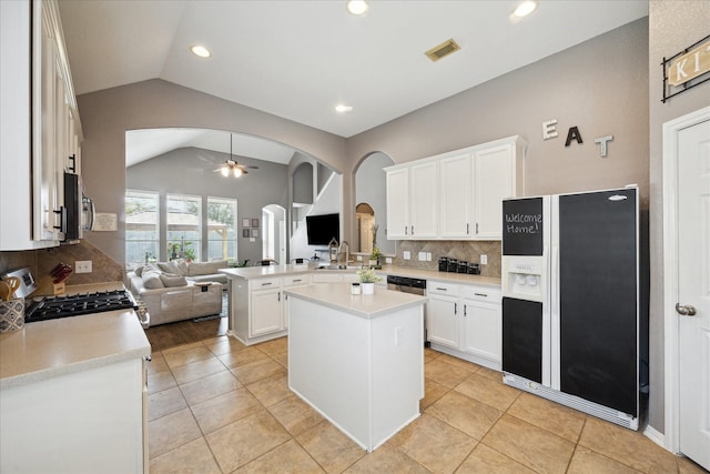 kitchen featuring arched walkways, appliances with stainless steel finishes, open floor plan, a peninsula, and vaulted ceiling