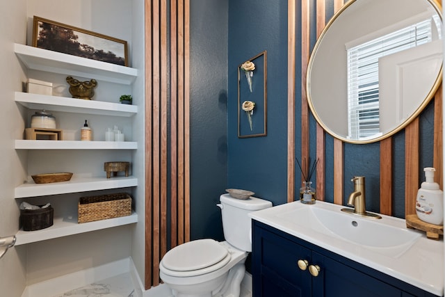 half bath featuring toilet, marble finish floor, baseboards, and vanity