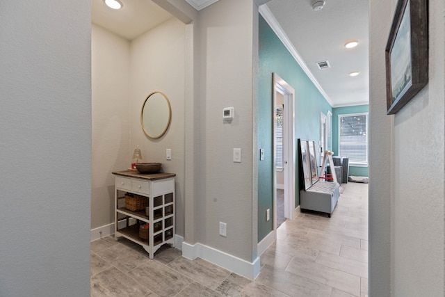 corridor with a textured wall, visible vents, crown molding, and baseboards