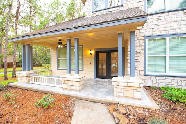 property entrance featuring a shingled roof, stone siding, ceiling fan, covered porch, and french doors