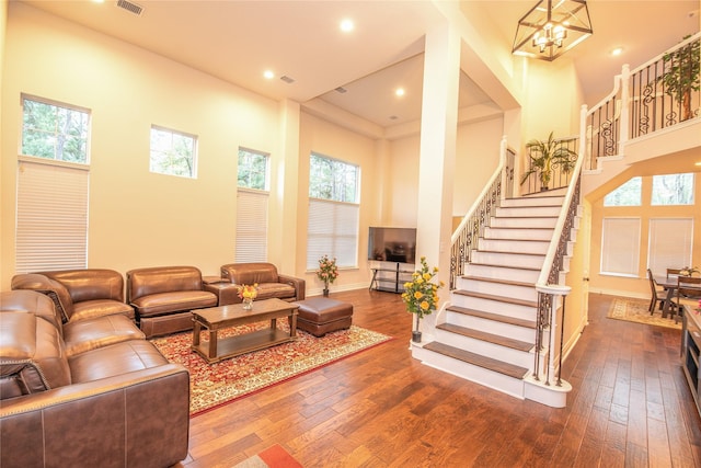 living room featuring a chandelier, a high ceiling, a healthy amount of sunlight, stairway, and hardwood / wood-style floors