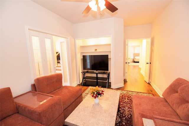 living area with a ceiling fan, stairs, baseboards, and wood finished floors