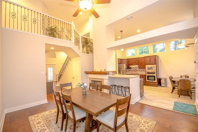 dining space with visible vents, stairway, a towering ceiling, light wood-style floors, and baseboards