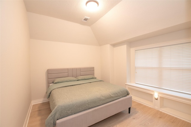 bedroom featuring light wood-type flooring, baseboards, visible vents, and vaulted ceiling