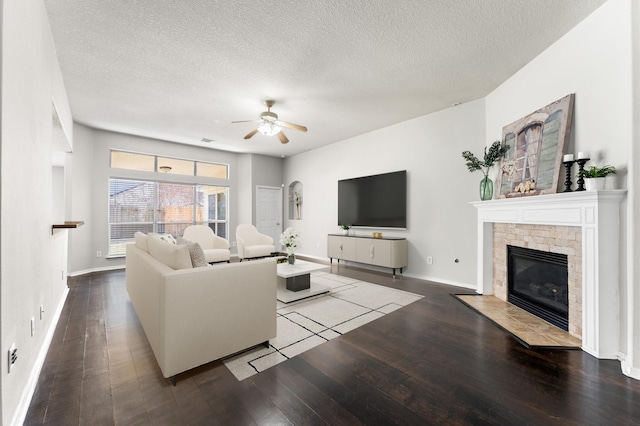 living area with ceiling fan, a textured ceiling, a fireplace with flush hearth, baseboards, and wood-type flooring